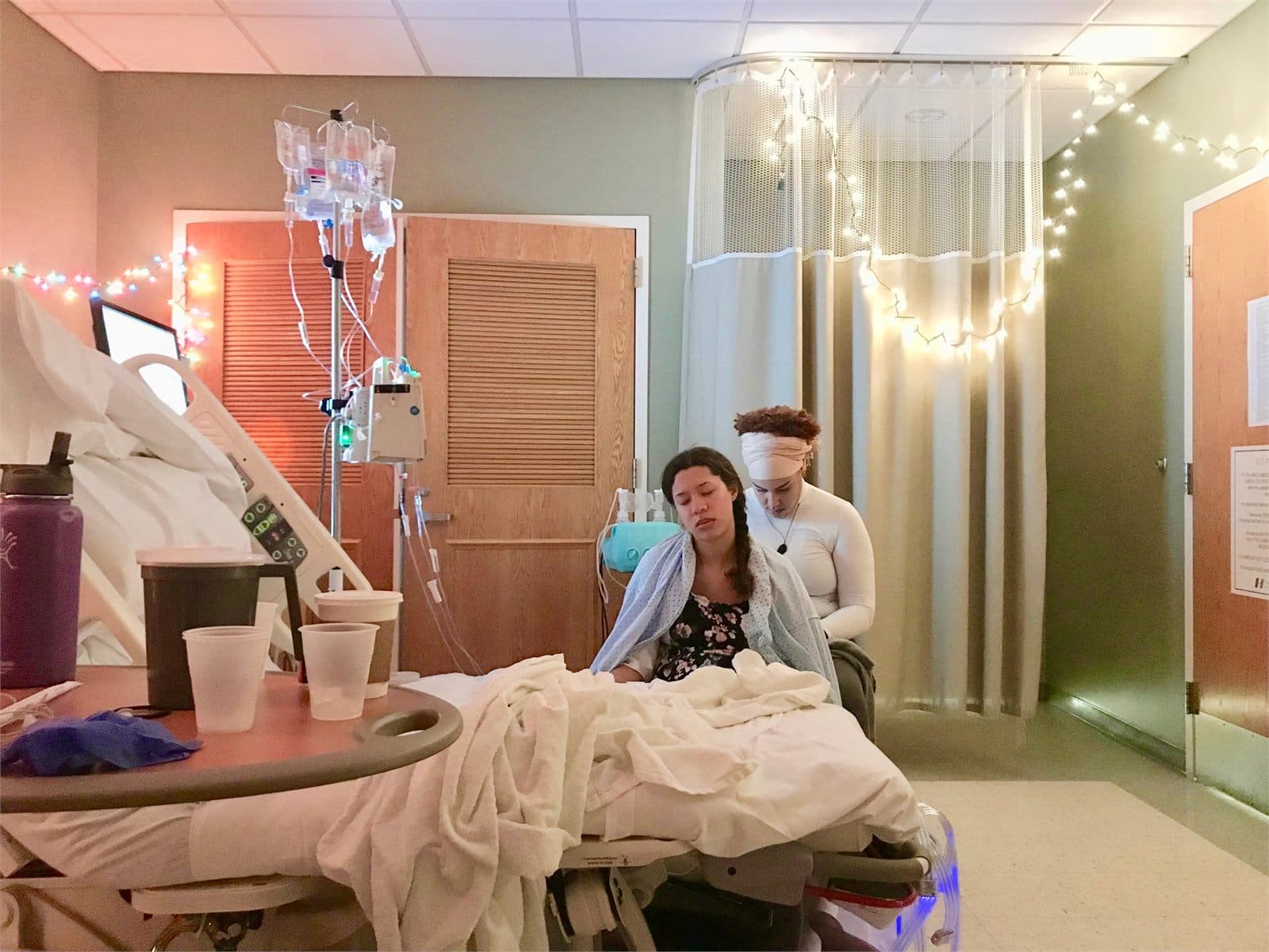 A labouring parent resting with their partner in a hospital birth room strung with fairy lights