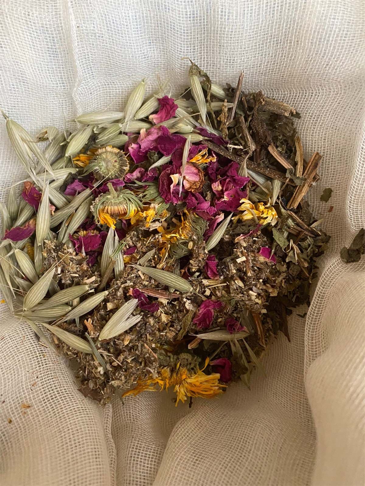 Dried rose petals, calendula and oat tops gathered on muslin for a herbal bath