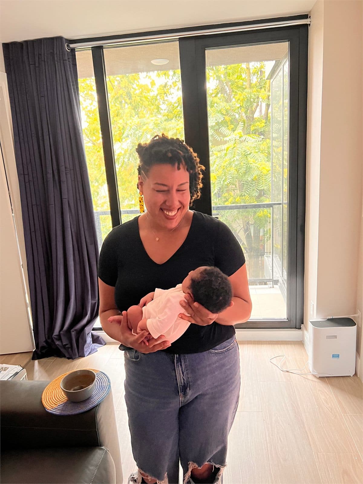 Valencia smiling while holding a swaddled newborn in a sunlit room