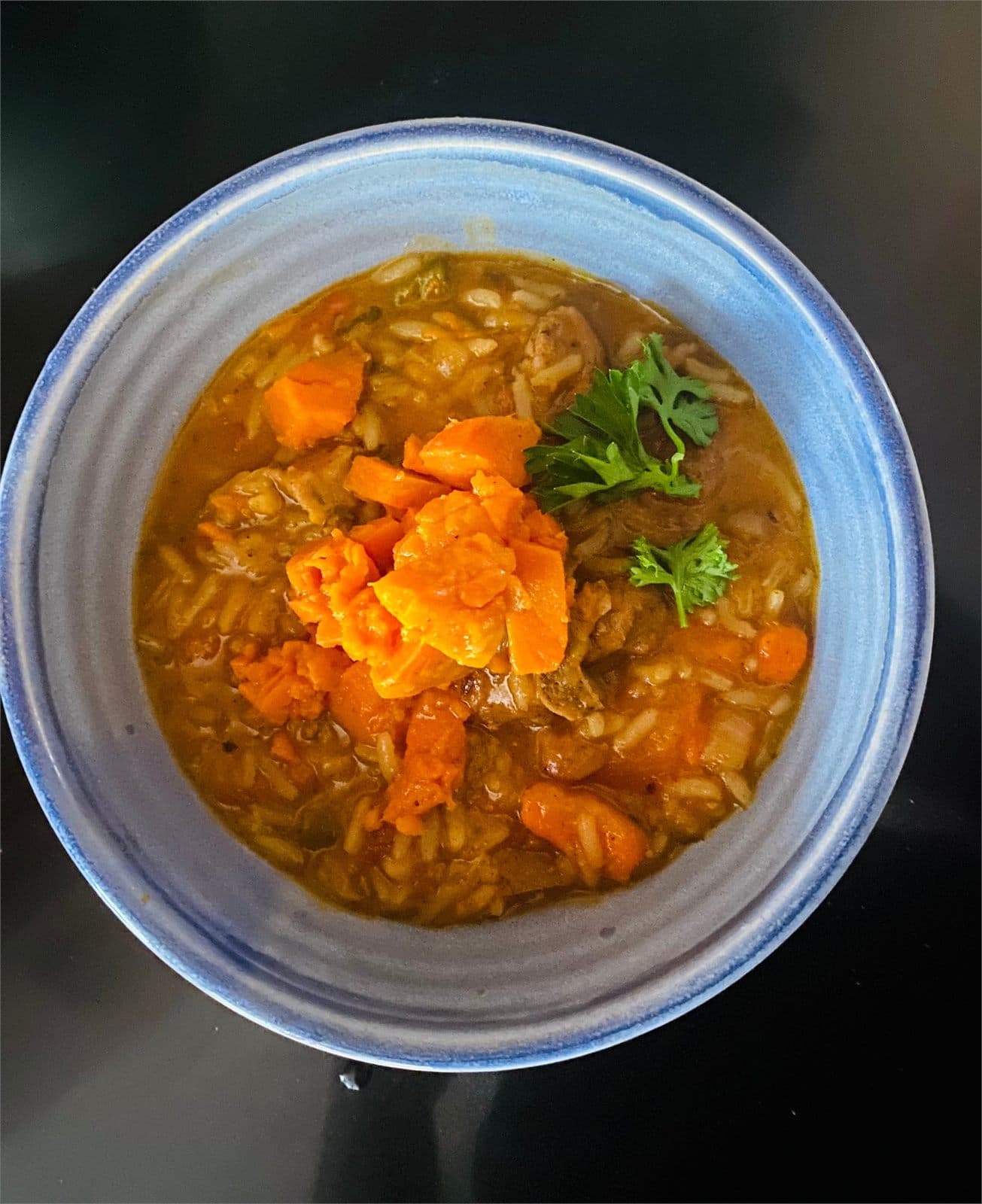 A bowl of sweet potato, carrot and rice soup garnished with parsley
