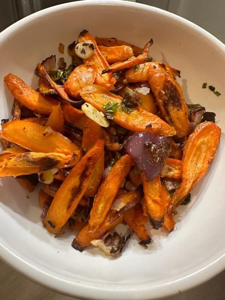 Roasted carrots with red onion and fresh herbs in a white bowl